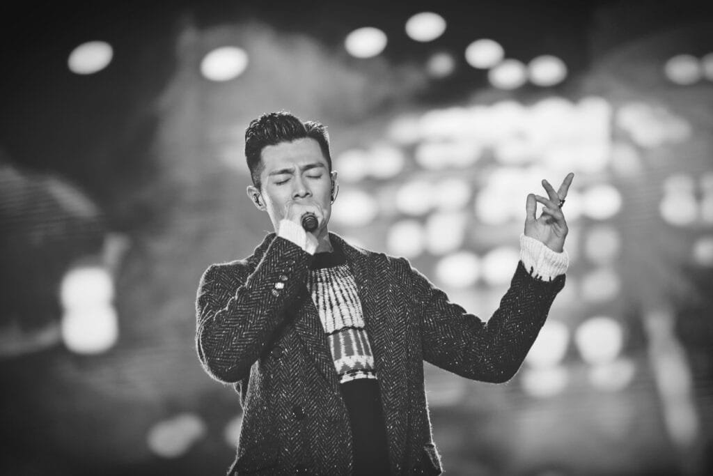A male singer passionately performs on stage under spotlights, creating a moody atmosphere.